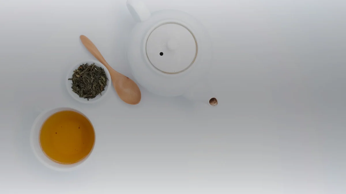 Thé vert en feuilles, théière blanche, cuillère en bois et tasse de thé doré vus de dessus