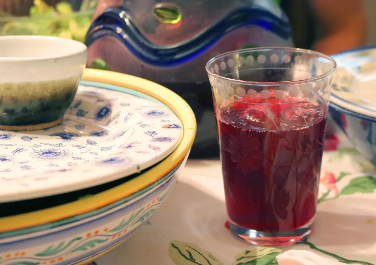 Verre d’infusion d’hibiscus rouge rubis posé sur une table, à côté d’assiettes en faïence